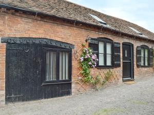 un bâtiment en briques avec une porte noire et des fleurs dans l'établissement The Smithy, à Little Witley