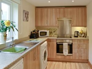 a kitchen with wooden cabinets and a sink and a microwave at Hen Ysgubor - 29518 in Fairbourne