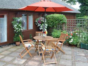 una mesa y sillas con una sombrilla en el patio en Church Barn Studio en Brundall