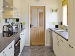 a kitchen with white cabinets and a wooden door at Woodlanders - 29954 in Wootton Glanville