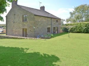 an old stone house with a grass field in front of it at Holly Bank in Crich