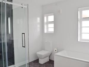 a white bathroom with a toilet and a glass shower at Windways in Port Erin