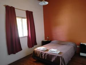 1 dormitorio con 1 cama y una ventana con cortinas rojas en Departamentos Turísticos El Coyote en San Rafael