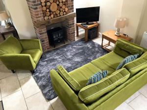 Grooms Cottage - E5398 في Dunstall: غرفة معيشة بها كنبتين خضراء وموقد