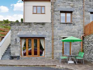 a stone house with a table and a green umbrella at Llwyn Rhedyn in Blaenau-Ffestiniog