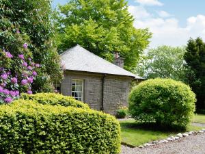 una pequeña casa de piedra en un jardín con arbustos en Dunlappie Lodge en Edzell
