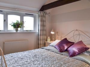 a bedroom with a bed with purple pillows and two windows at Maplehurst Barn Stables in Staplehurst