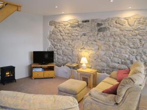 a living room with a stone wall and two couches and a tv at The Old Coach House in St Austell