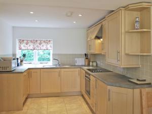 cocina con armarios de madera, fregadero y ventana en Winhill Cottage, en Bamford