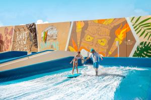 un hombre y una mujer montando una ola en una tabla de surf en el agua en Dreams Vista Cancun Golf & Spa Resort en Cancún