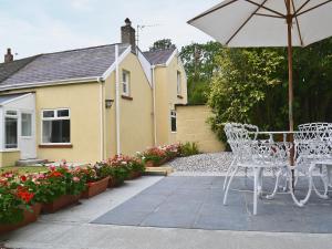 a patio with a table and an umbrella and flowers at Bont Cottage in Kidwelly
