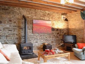 a living room with a stone wall with a stove at Ty Coch Cottage in Dihewid