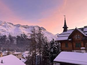 a church with a snow covered roof with mountains in the background at New! Exclusive Apartment 3min to Chantarella Bahn in St. Moritz