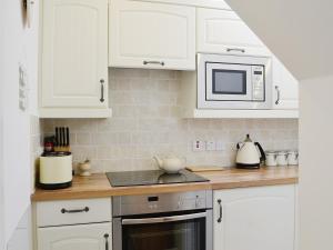 cocina con armarios blancos, fogones y microondas en Song Bird Cottage, en Lochend