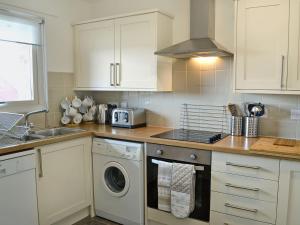 cocina con armarios blancos, lavadora y secadora en Sandy View, en Beadnell