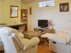 a living room with two white chairs and a tv at The Stables in Dunterton