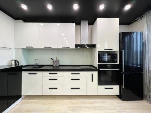 a kitchen with white cabinets and a black refrigerator at Апартаменты LUX + in Pavlodar