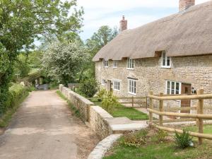 an old stone house with a thatched roof and a dirt road at The Farmhouse At Higher Westwater in Axminster