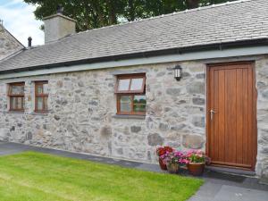 a stone cottage with a wooden door and some flowers at Seion - Hw7575 in Llanddeiniolen