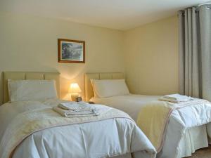 a bedroom with two beds with white sheets and a lamp at Caroch Cottage in Comrie