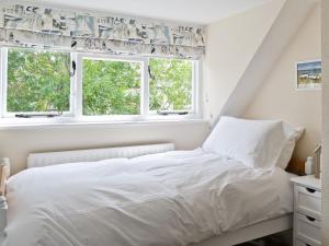 a bedroom with a white bed and two windows at Tennay Cottage in Wareham