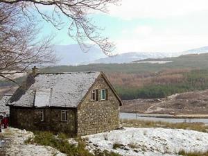 una vieja casa de piedra sentada en una colina cubierta de nieve en Tigh Na Caoiraich en Tomdoun