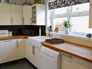 a kitchen with white cabinets and a sink and a window at Mackenzie Cottage in Poolewe