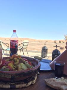 una mesa con una sartén de comida y una botella de coca en BerberNightCamp, en Adrouine