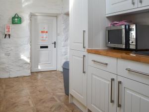 a kitchen with white cabinets and a microwave at Porth Cormon Farmhouse in Llangwnadl
