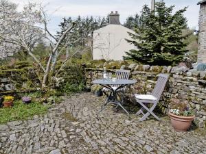 a table and chairs in a garden with a stone wall at Greystones Cottage in Hardraw