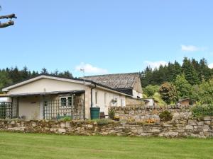 a house with a stone fence in front of a yard at Fir Tree Cottage - Ukc646 in Byrness