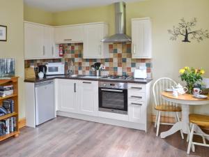 a kitchen with white cabinets and a table at Fir Tree Cottage - Ukc646 in Byrness