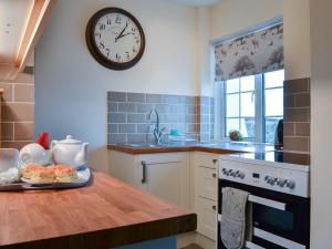 cocina con reloj en la pared y mesa en St Cadoc Cottage, en St Merryn