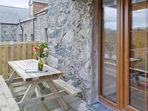 a wooden picnic table on a patio with a stone wall at Rhiwal Kitty in Bodedern
