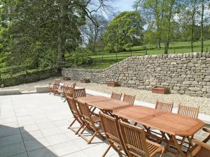 una fila de mesas y sillas de madera junto a una pared de piedra en Tythe Barn, en Froggatt