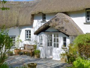 Cabaña con techo de paja y banco frente a ella en The Thatch Cottage en South Petherwin