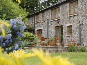 een stenen huis met stoelen en bloemen in de tuin bij Grooms Cottage in Westleigh