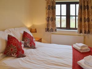 um quarto com uma cama branca com almofadas vermelhas e uma janela em The Cart Shed em High Halstow