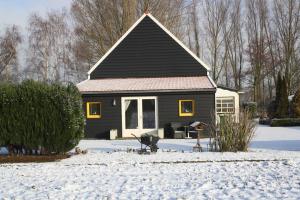 una casa con un tetto nero nella neve di De Nieuwe Stal a Scherpenisse