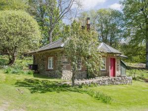 Katys Cottage في Balnaboth: منزل حجري بباب احمر في ساحة