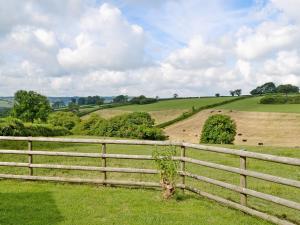 a wooden fence in a field with animals in the distance at Woods Cottage in Evershot