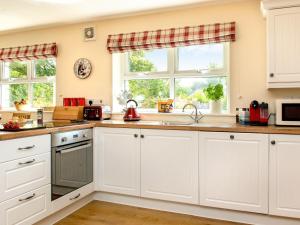 a kitchen with white cabinets and a sink and two windows at Blackberry Cottage in North Hill