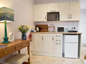 eine Küche mit weißen Schränken und einem Schreibtisch mit einer Mikrowelle in der Unterkunft Little Croxley in Wroxall