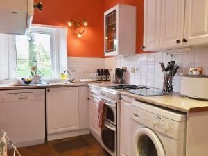 a kitchen with white cabinets and an orange wall at Birch Cottage- 15841 in Catcleugh