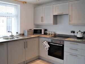 a kitchen with white cabinets and a sink and a microwave at Freya Cottage in Flamborough