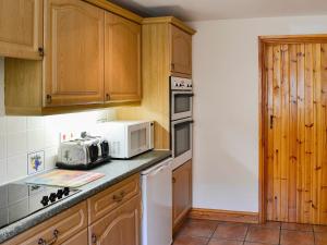cocina con armarios de madera y microondas blanco en Carters Cottage, en Puncknowle