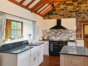 a kitchen with white cabinets and a stone wall at The Wee Byre in Shawhead