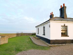 a white building with a grassy yard next to a wall at Lighthouse Cottage in Happisburgh