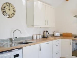 a kitchen with white cabinets and a clock on the wall at The Garden Cottage in Wrangaton