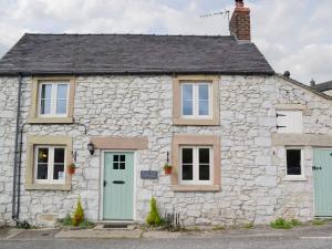 a stone cottage with green doors and windows at Dale End Cottage in Brassington
